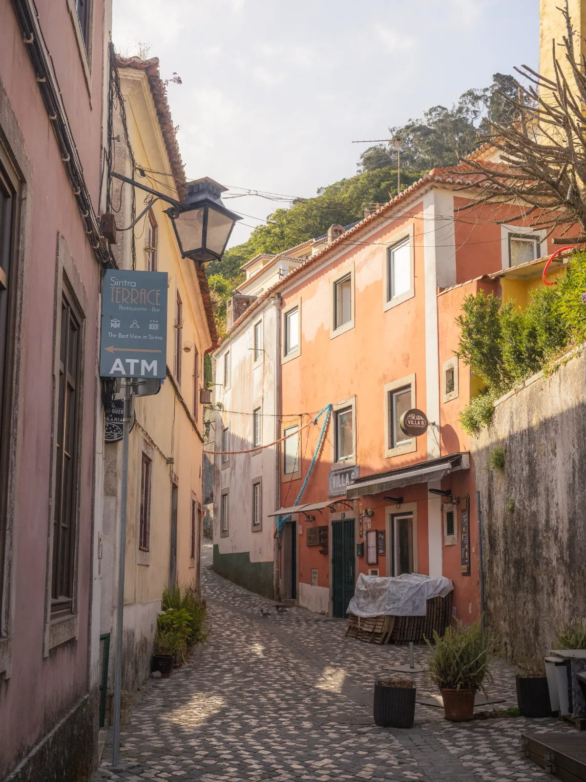Cobbled lane in Sintra's old town with pastel houses and a palace tower above the trees